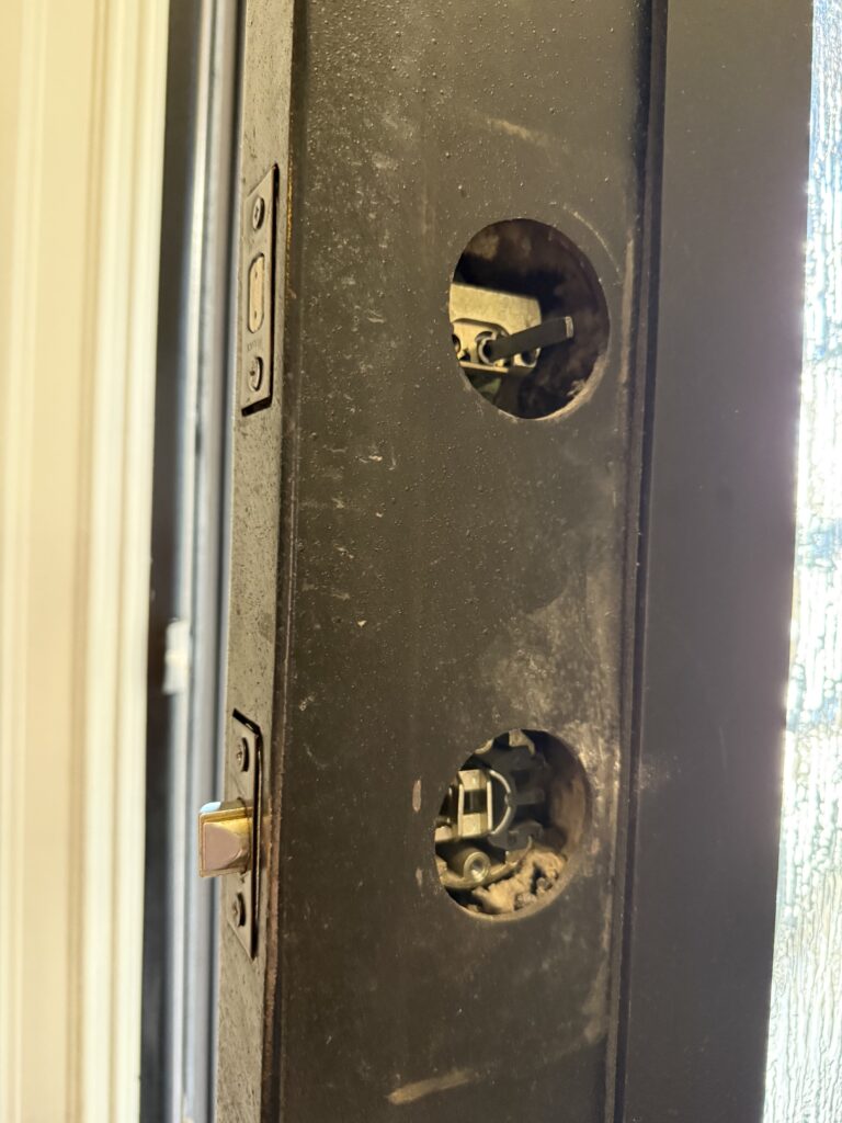Lock mounting openings exposed on a metal front door during latch replacement in Broken Arrow